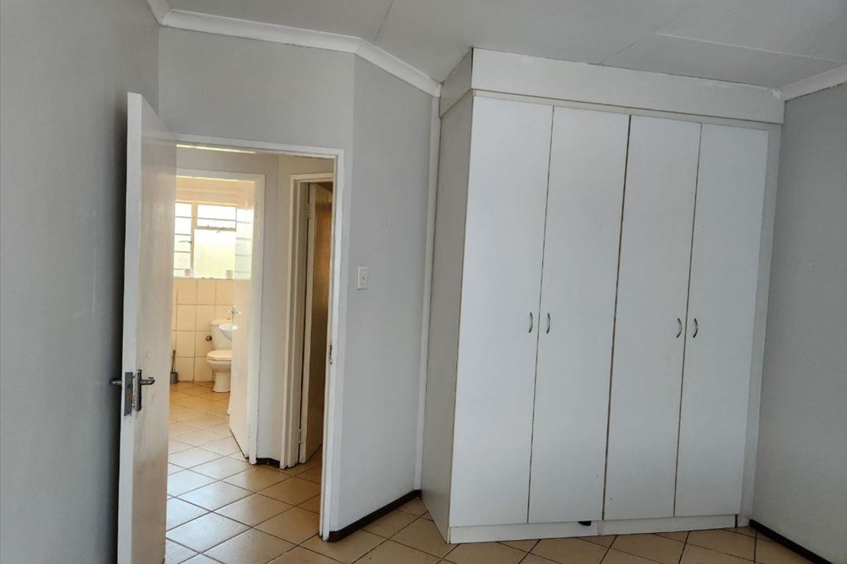 A vacant bedroom featuring built-in wardrobes, tiled flooring, and direct access to an adjacent bathroom.