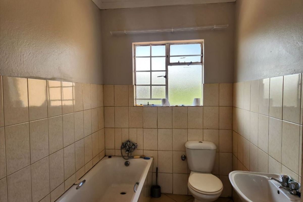 A dated bathroom featuring a standard bathtub, pedestal basin, and toilet with tiled walls and flooring, requiring cosmetic updates to modernize the space.