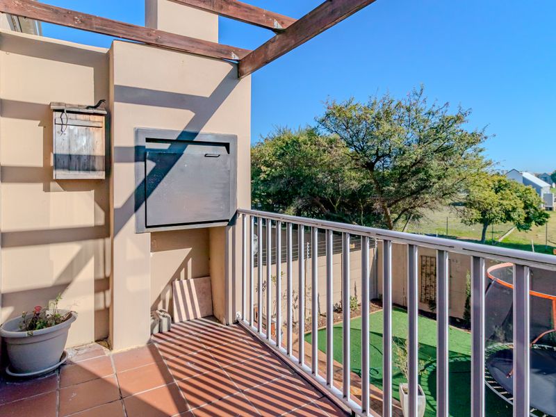 A private balcony featuring a built-in braai, timber pergola, and tiled flooring, overlooking the garden area.