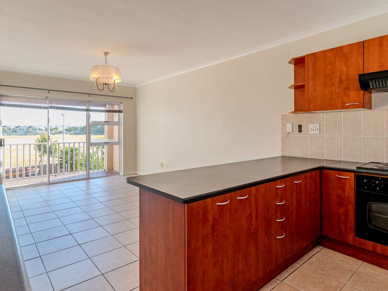 Open-plan kitchen and living area featuring wooden cabinetry, dark countertops, and direct access to a balcony through sliding glass doors.
