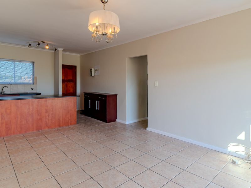 Open plan living and kitchen area featuring tiled flooring, wooden cabinetry, a kitchen island with a built-in hob, and neutral wall finishes.