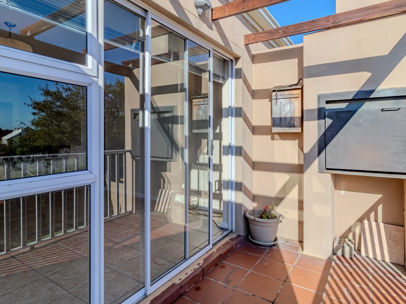 A covered balcony featuring tiled flooring, a built-in braai, and a timber pergola, offering an ideal space for outdoor entertaining.