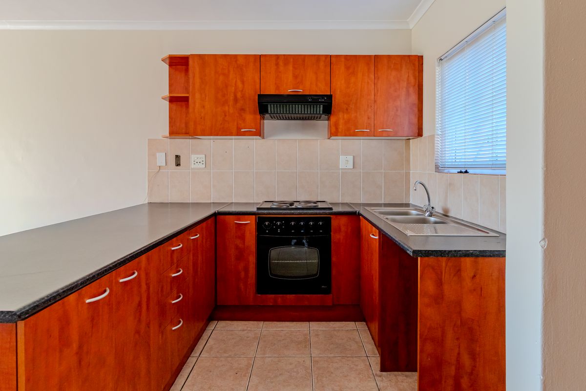 A functional kitchen featuring wood-finish cabinetry, dark countertops, built-in oven and hob, tiled splashback, and a double bowl sink.