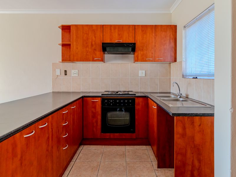 A functional kitchen featuring wood-finish cabinetry, dark countertops, built-in oven and hob, tiled splashback, and a double bowl sink.