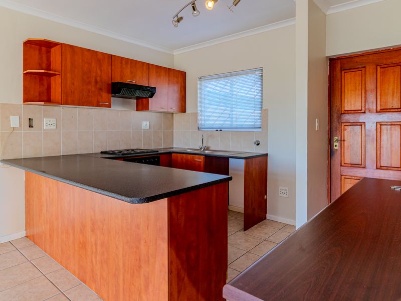 A functional kitchen featuring wood-look cabinetry, dark countertops, a built-in hob with extractor, and tiled flooring in an open-plan layout.