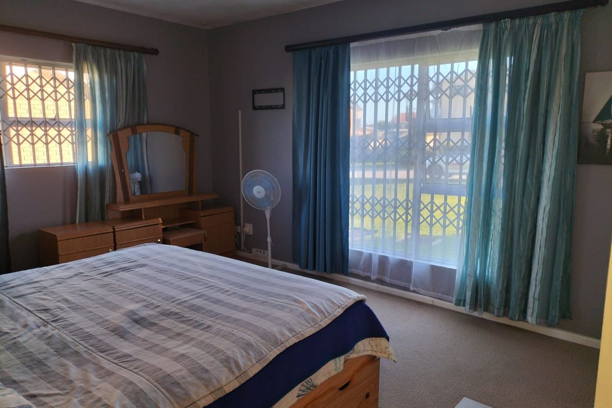 A spacious bedroom featuring carpeted flooring, large windows with security gates, and curtain rods, offering a functional and comfortable living space.