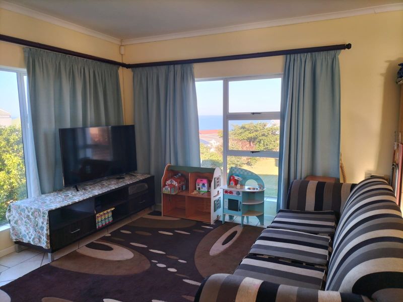 A bright living room featuring large windows with views, tiled flooring, and neutral wall finishes, offering a comfortable space for relaxation.