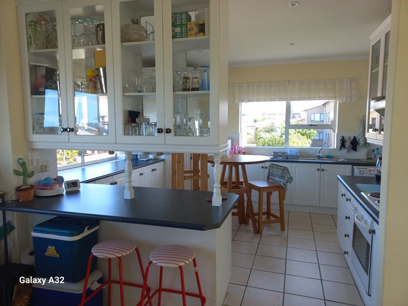 Functional kitchen featuring white cabinetry, glass-fronted display units, dark laminate countertops, built-in oven, and tiled flooring with a breakfast bar area.