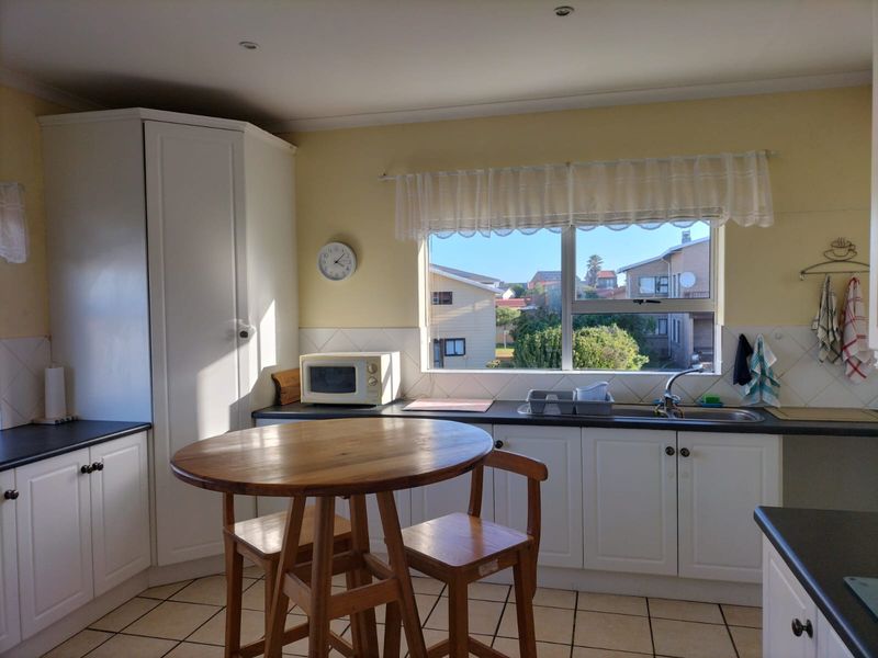 A functional kitchen featuring white cabinetry, dark laminate countertops, tiled flooring, and a window overlooking the neighbourhood.
