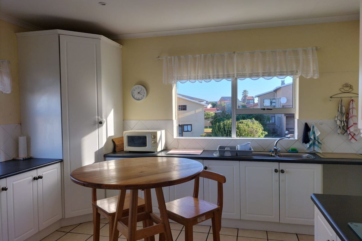 A functional kitchen featuring white cabinetry, dark laminate countertops, tiled flooring, and a window overlooking the neighbourhood.