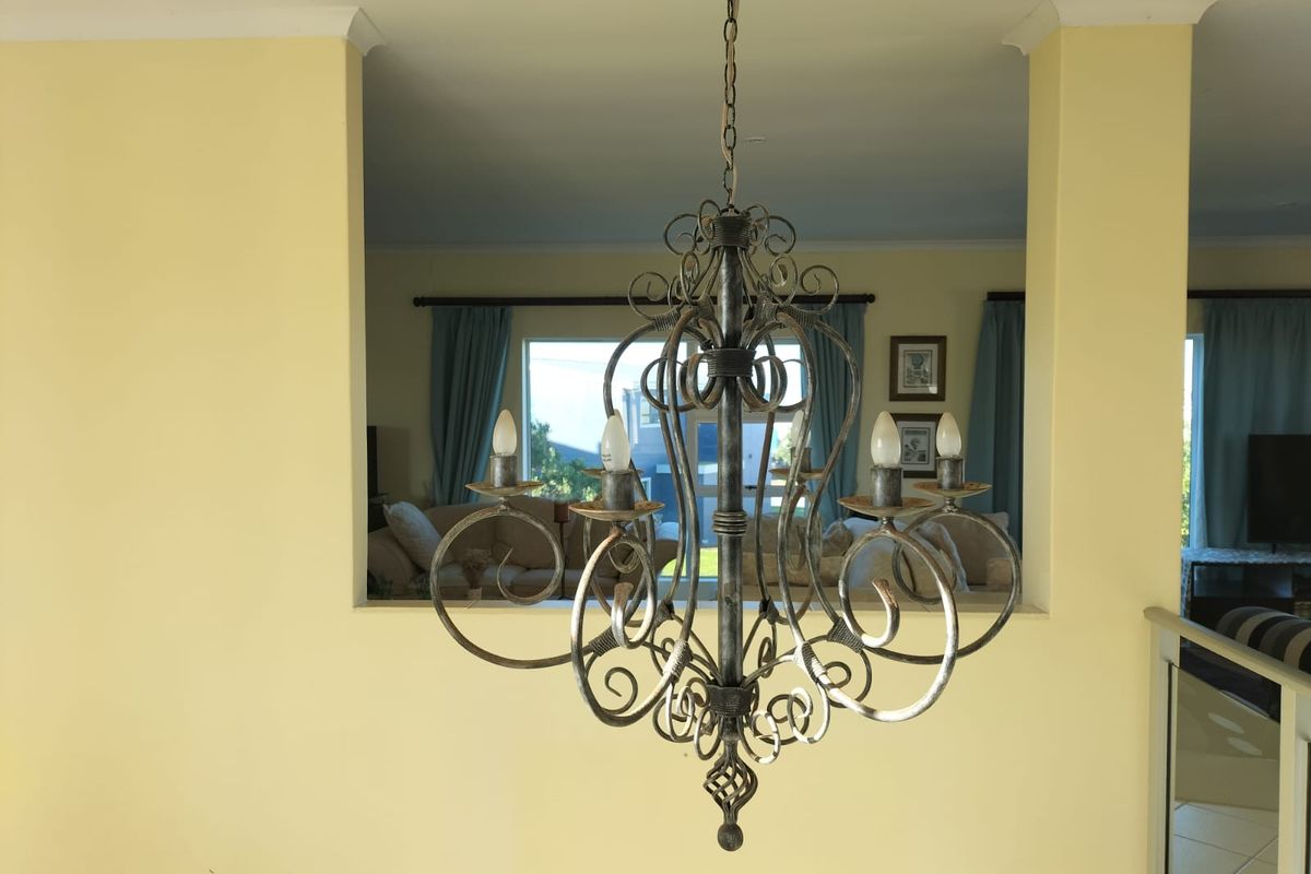 A view through a pass-through window into a living area, featuring a decorative wrought iron chandelier and yellow wall finishes.