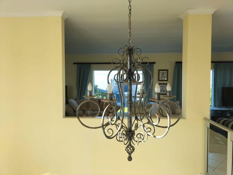 A view through a pass-through window into a living area, featuring a decorative wrought iron chandelier and yellow wall finishes.