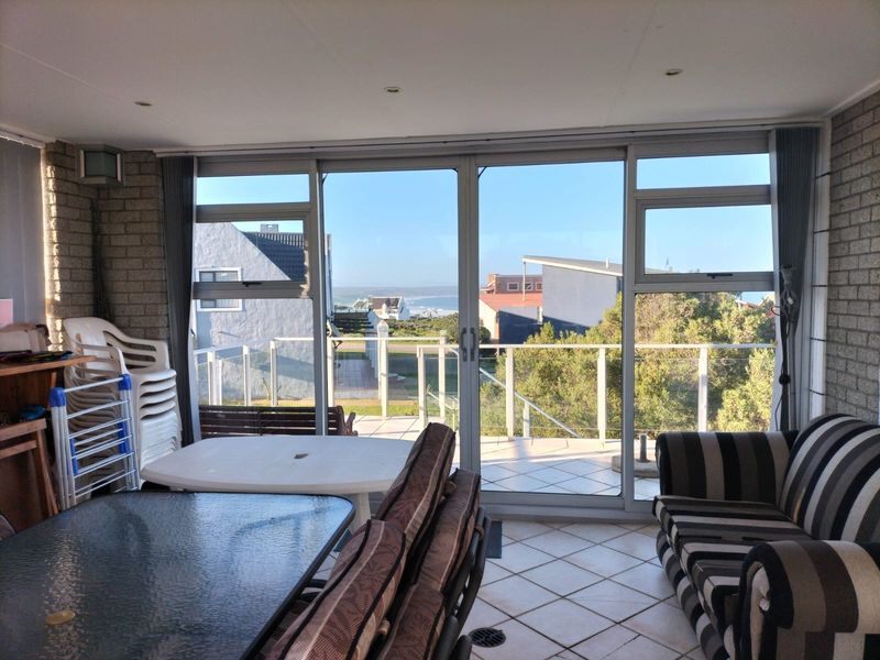 Enclosed patio area featuring tiled flooring, exposed brick walls, and large sliding glass doors offering views of the surrounding neighborhood and distant coastline.