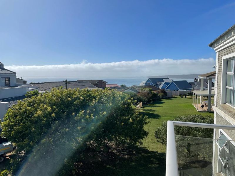 Elevated coastal view overlooking the surrounding neighbourhood and ocean horizon, captured from a balcony with a modern glass balustrade.