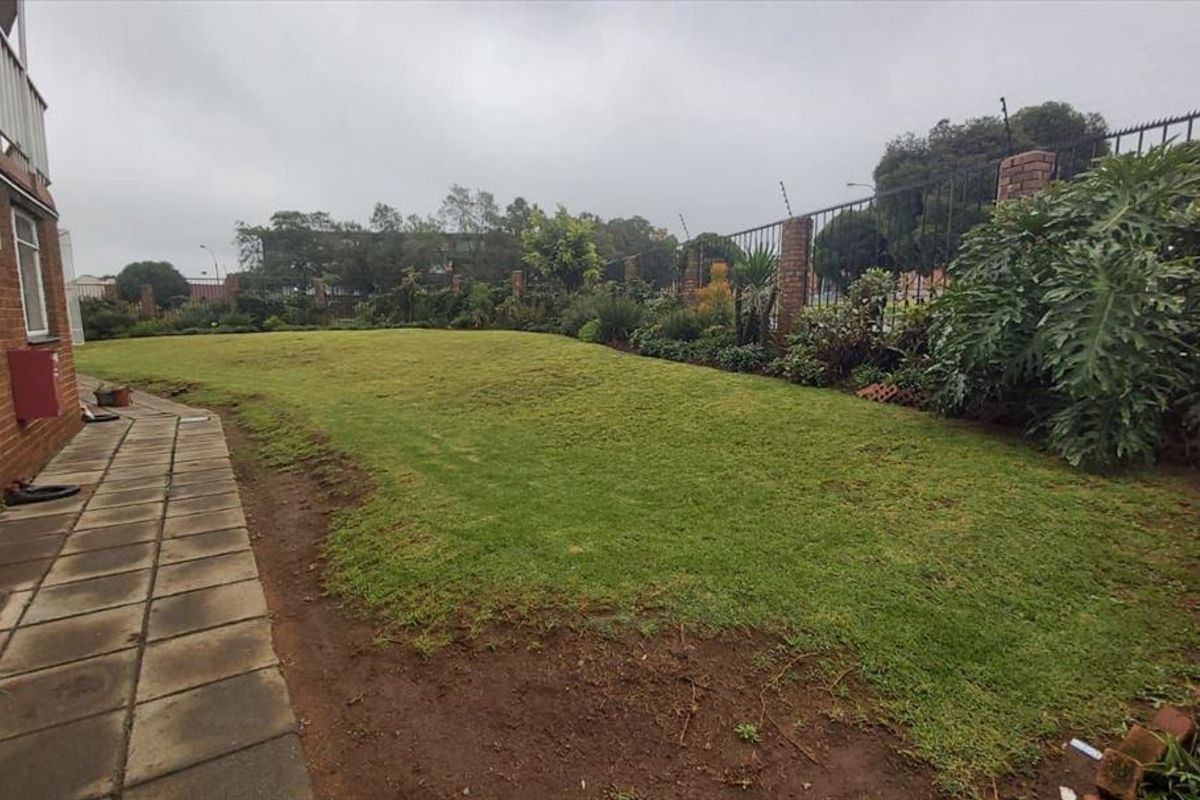A private rear garden area featuring a paved walkway, established lawn, and secure perimeter wall with electric fencing.