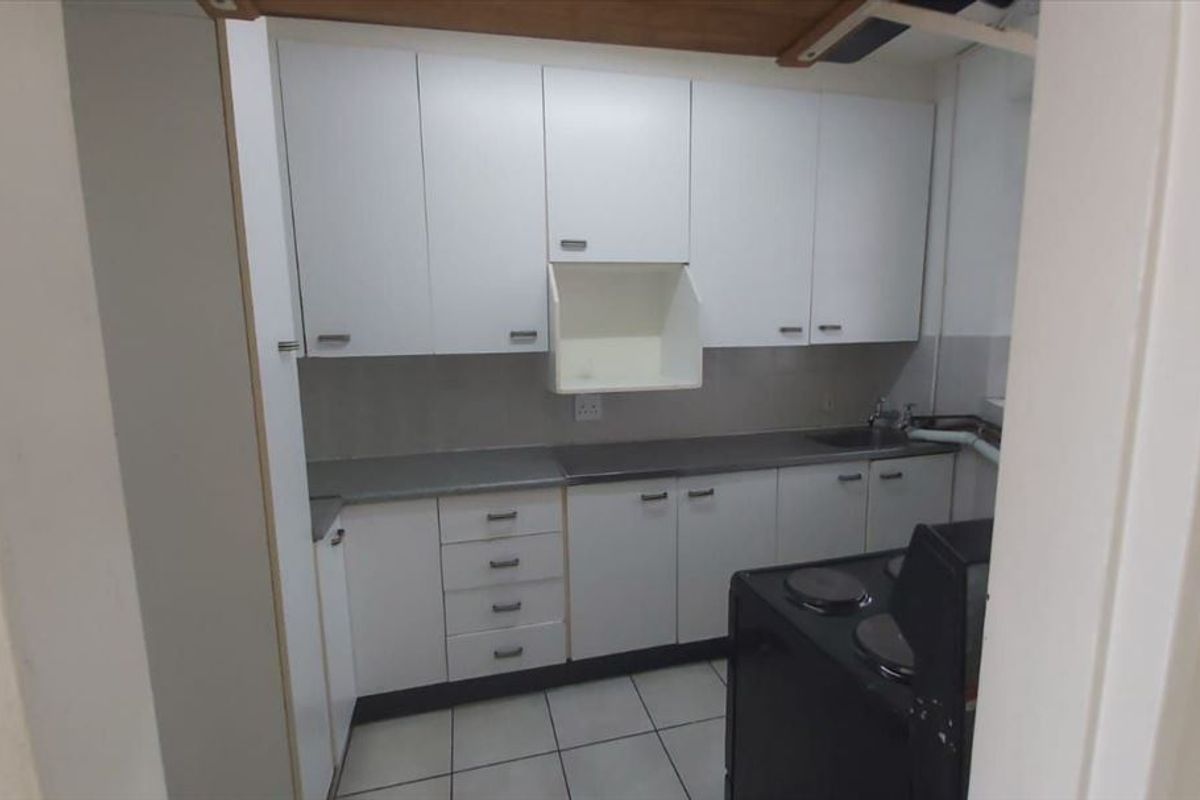 A compact, functional kitchen featuring white cabinetry, tiled flooring, and a tiled splashback, offering a clean canvas for potential modern updates.