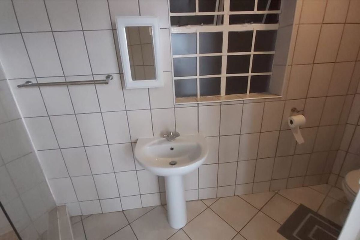 A functional bathroom featuring a pedestal basin, shower enclosure, and toilet, finished with neutral wall and floor tiles.