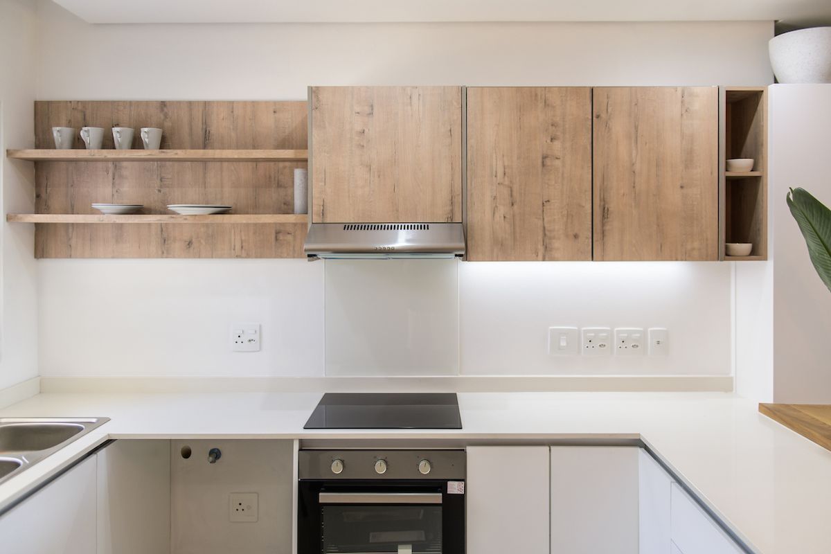 Modern kitchen featuring light wood-look cabinetry, stone countertops, integrated electric hob, oven, extractor fan, and open shelving with under-cabinet lighting.