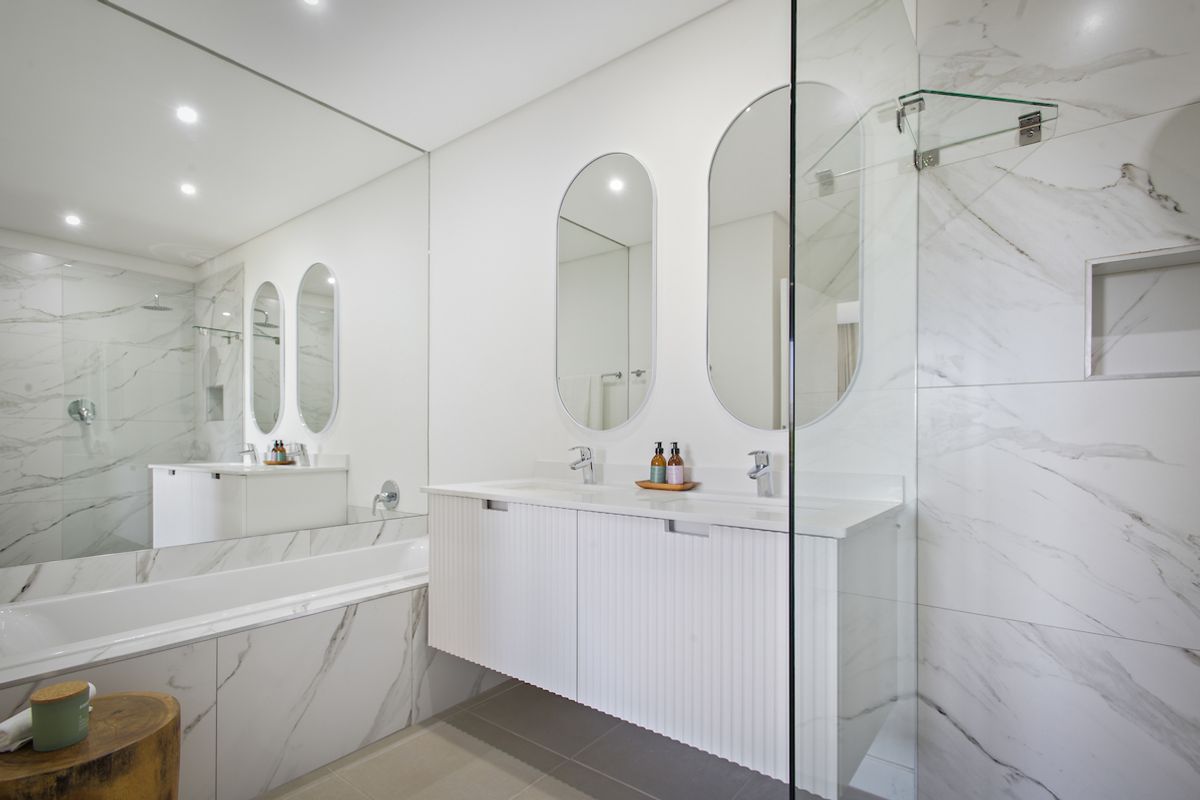 Modern bathroom featuring a double vanity with fluted cabinetry, marble-look wall tiles, a built-in bathtub, and a glass-enclosed shower with a recessed niche.