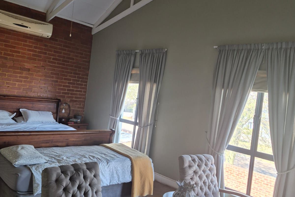 Spacious bedroom featuring a high vaulted ceiling with exposed trusses, an exposed brick feature wall, and large windows providing ample natural light.