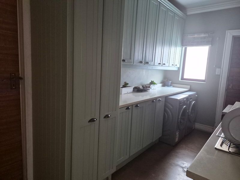 A functional laundry room featuring extensive built-in cabinetry, ample countertop workspace, and a window for natural light.