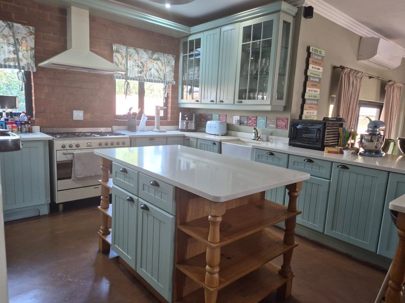 A charming country-style kitchen featuring light blue cabinetry, a central island with stone countertops, a farmhouse sink, and an exposed brick feature wall.