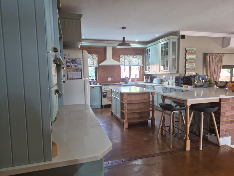 Spacious kitchen featuring a central island, exposed brick accents, light blue cabinetry, stone countertops, and polished concrete flooring.