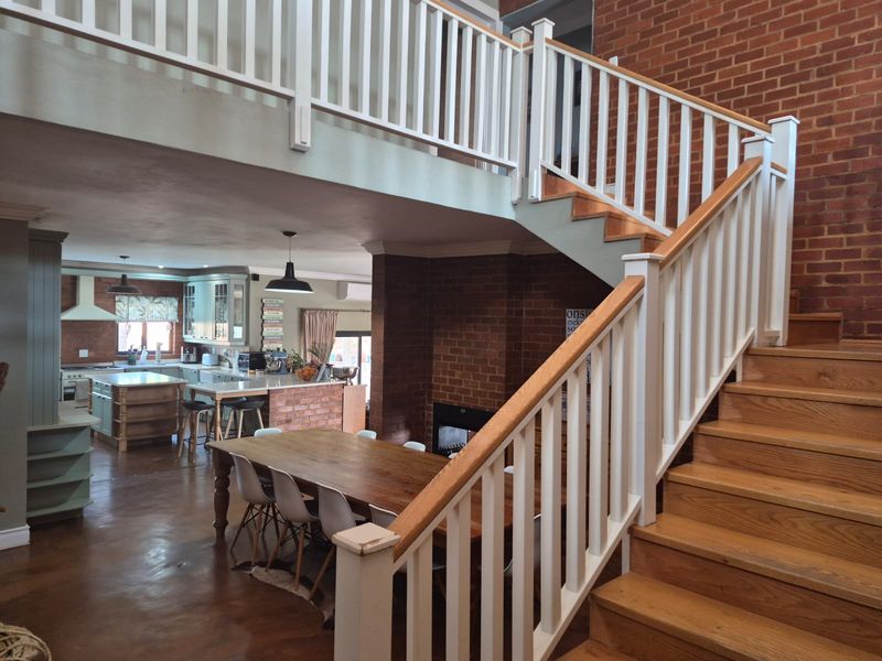 Spacious open-plan living area featuring a striking timber staircase, exposed brickwork, a fireplace, and a well-appointed kitchen with a central island.