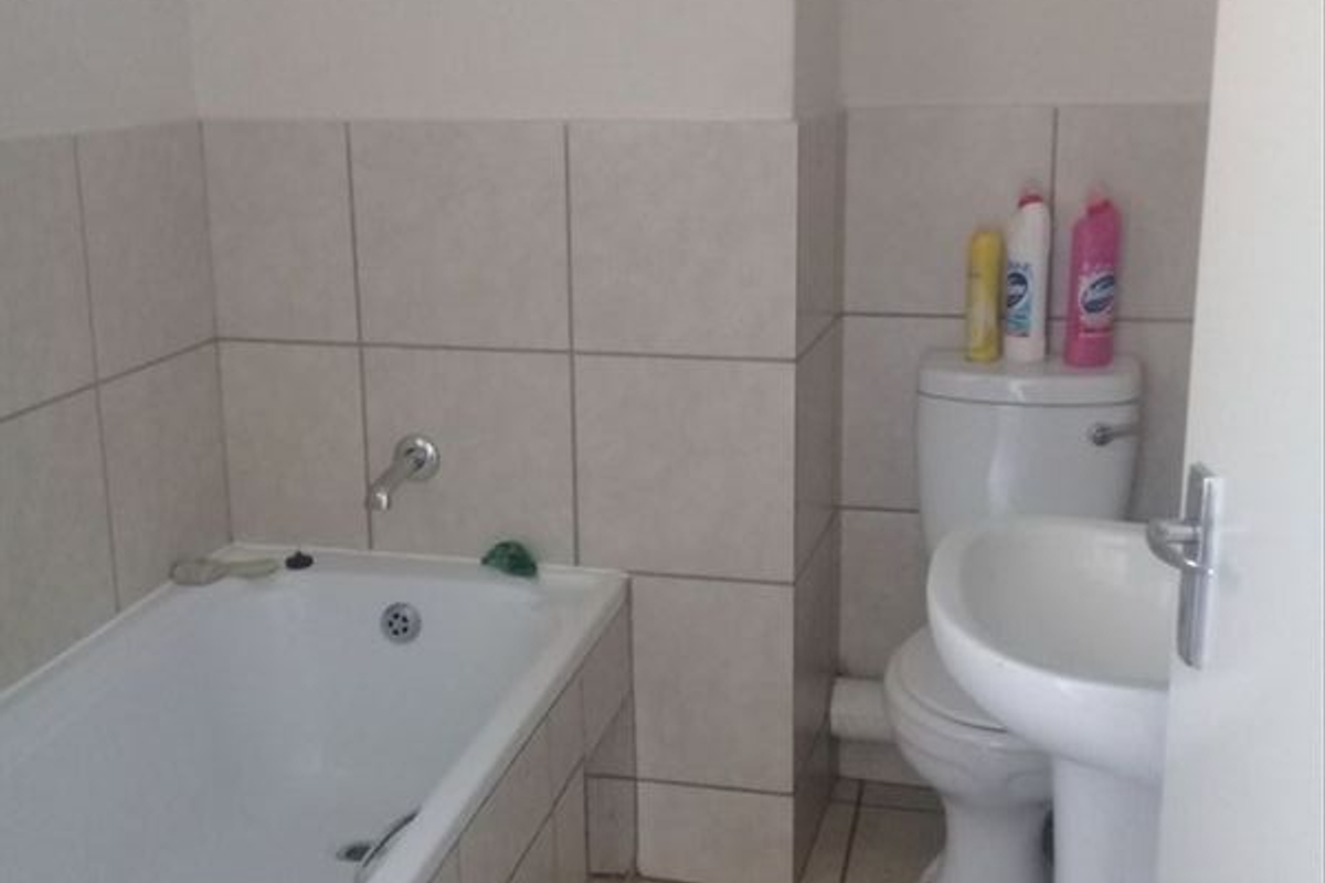 A functional bathroom featuring a bathtub, pedestal basin, and toilet with neutral ceramic wall and floor tiling.