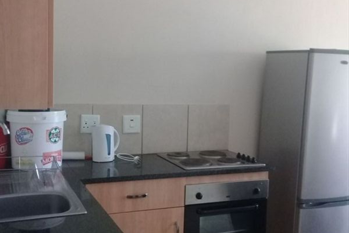 Compact kitchen featuring laminate cabinetry, granite countertops, built-in oven, electric hob, and tiled flooring.