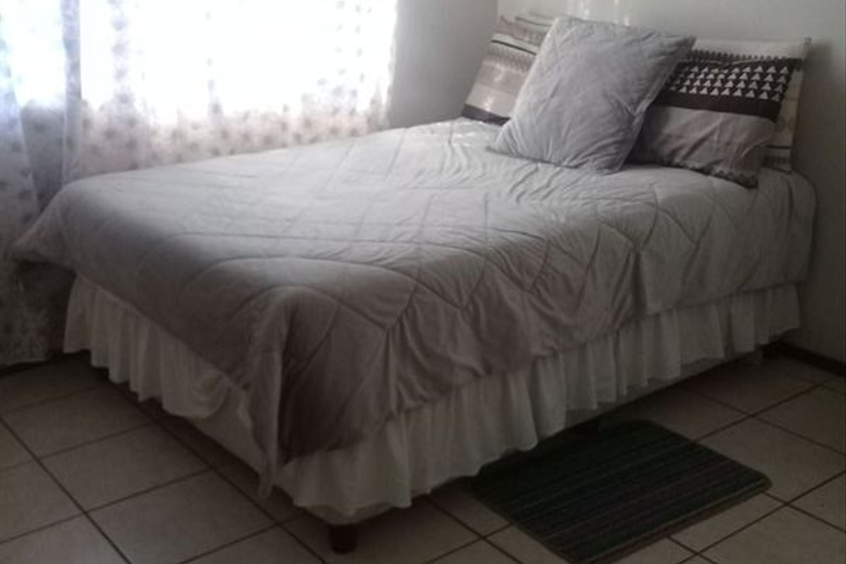 A simple bedroom featuring tiled flooring and natural light from the window.