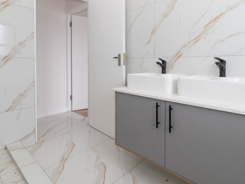 Modern bathroom featuring a double vanity with black fixtures, marble-look wall and floor tiles, and a spacious walk-in shower area.