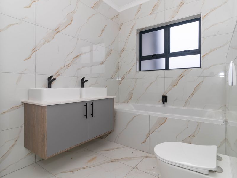 Modern bathroom featuring a double vanity with wall-mounted cabinetry, a built-in bathtub, and elegant marble-look tiling throughout.