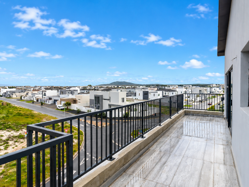 A spacious balcony featuring modern tiled flooring and a secure metal balustrade, offering expansive views of the surrounding residential neighborhood.