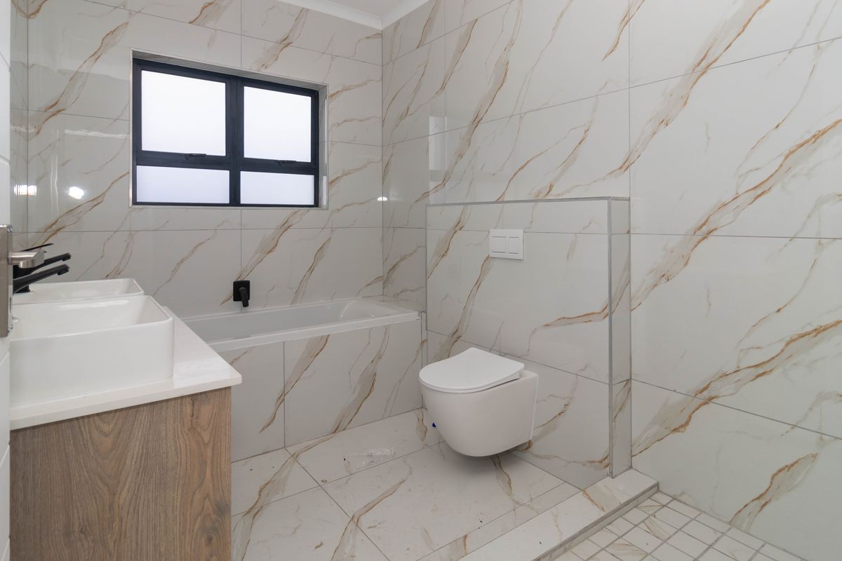 Modern bathroom featuring marble-look wall and floor tiles, a wall-mounted toilet, built-in bathtub, and a double vanity with contemporary black tapware.