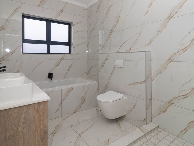 Modern bathroom featuring marble-look wall and floor tiles, a wall-mounted toilet, built-in bathtub, and a double vanity with contemporary black tapware.
