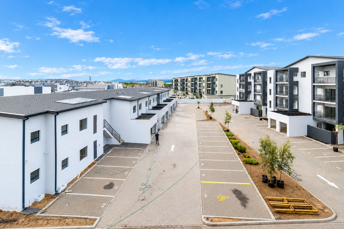 Aerial view of a modern apartment complex featuring paved parking bays, multi-story residential blocks with balconies, and ongoing landscaping work.