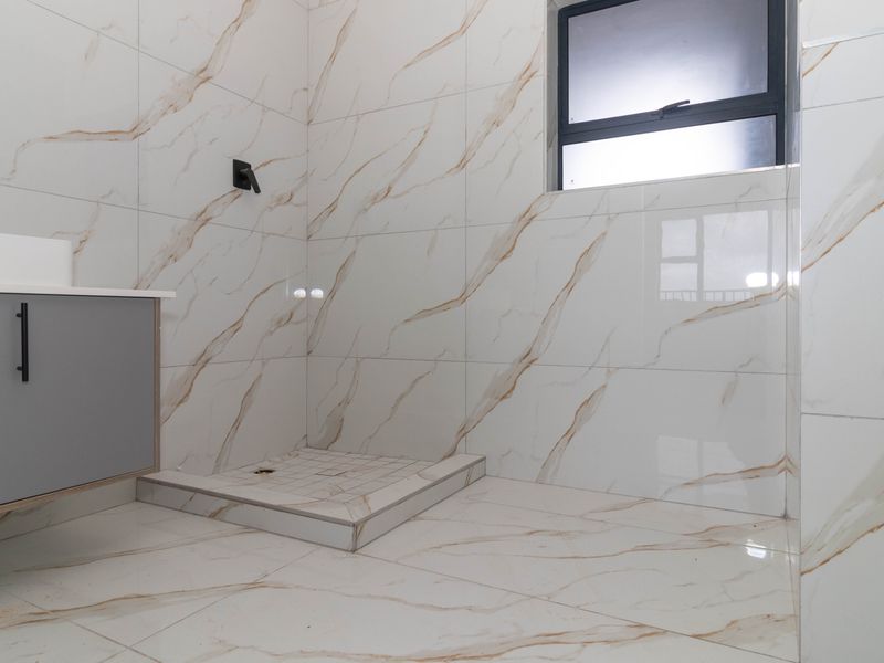 Modern bathroom featuring marble-look wall and floor tiles, a grey vanity cabinet with basin, and a walk-in shower area.