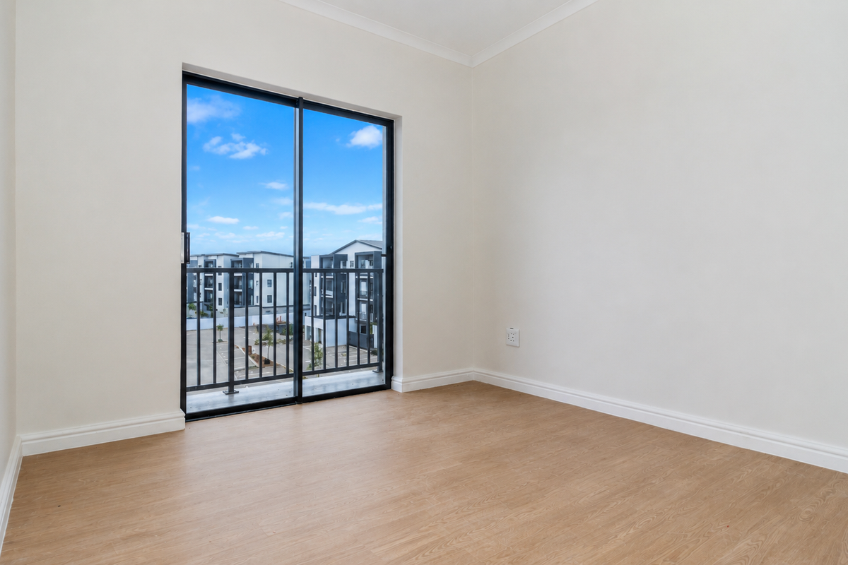 A bright, empty bedroom featuring modern laminate flooring, neutral walls, and a sliding glass door leading to a private balcony.