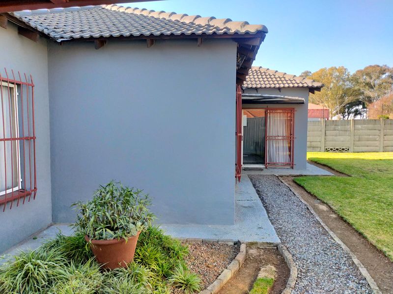 Rear exterior view of the house featuring a gravel pathway, lawn area, and security bars on the windows.