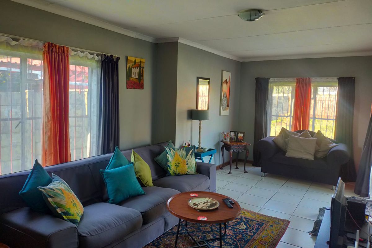 A spacious living room featuring neutral wall tones, tiled flooring, and large windows with security bars, providing ample natural light.