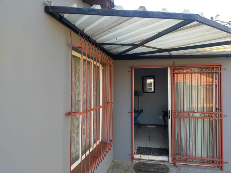 Covered patio area featuring a corrugated metal awning, security bars on windows and doors, and tiled flooring.