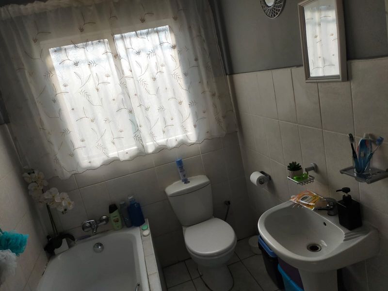 A functional bathroom featuring a bathtub, pedestal basin, and toilet with neutral wall tiling.