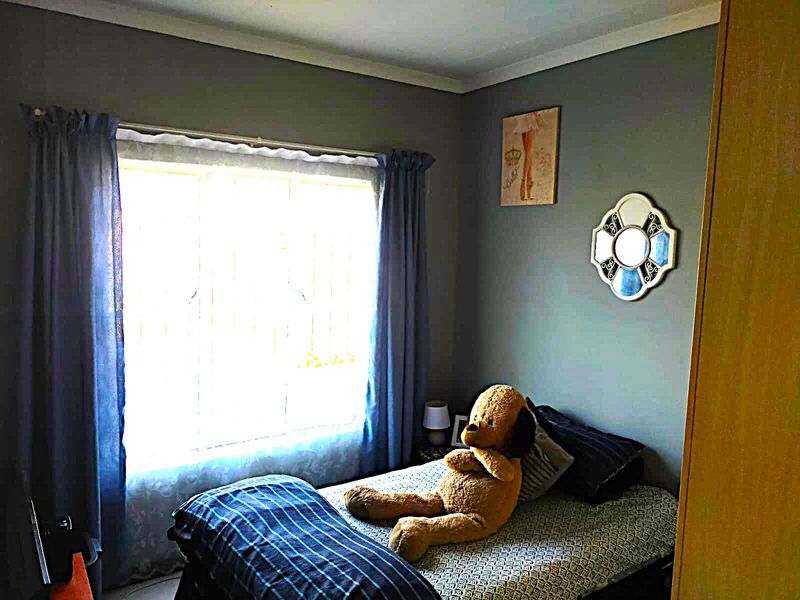 A cozy bedroom featuring a built-in wardrobe, a window with security bars, and neutral wall finishes.