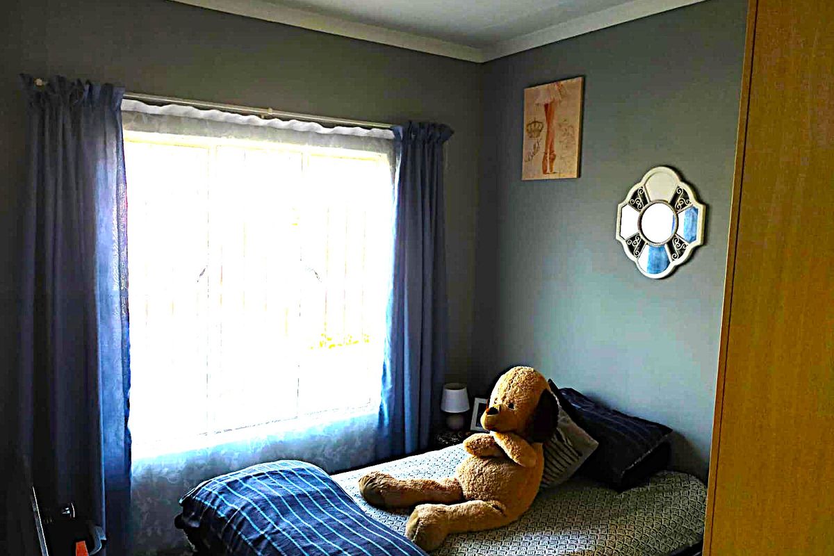 A cozy bedroom featuring a built-in wardrobe, a window with security bars, and neutral wall finishes.