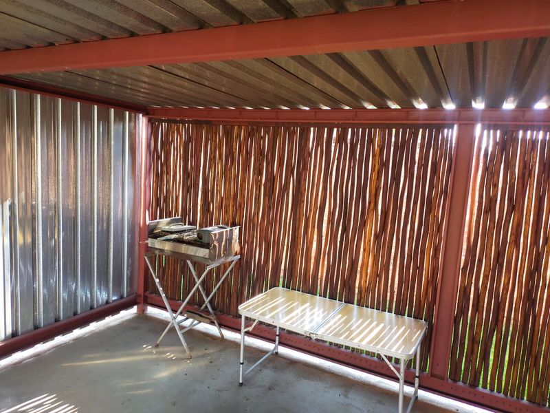 A covered outdoor patio area featuring a steel frame structure, corrugated metal roofing, and reed screening, providing a basic space for outdoor entertainment.