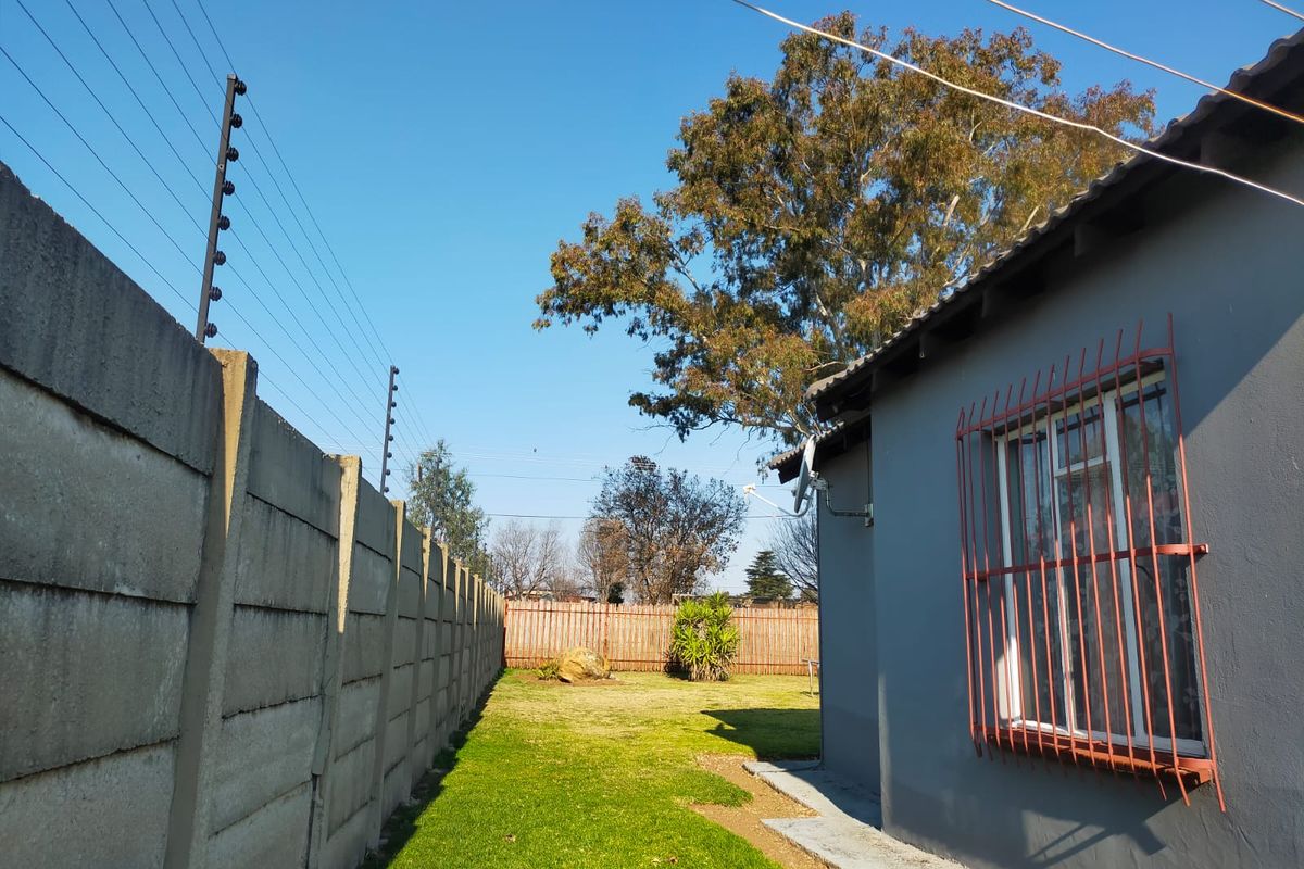 Rear garden area featuring a lawn, precast concrete boundary wall with electric fencing, and a side elevation of the house with security bars.