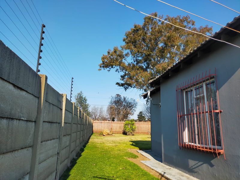Rear garden area featuring a lawn, precast concrete boundary wall with electric fencing, and a side elevation of the house with security bars.