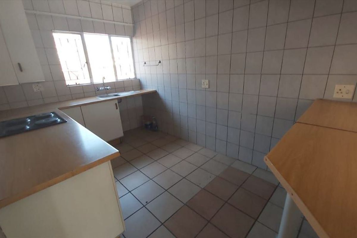 A functional, empty kitchen featuring tiled walls, laminate countertops, an integrated electric hob, and a stainless steel sink, ready for modernization.