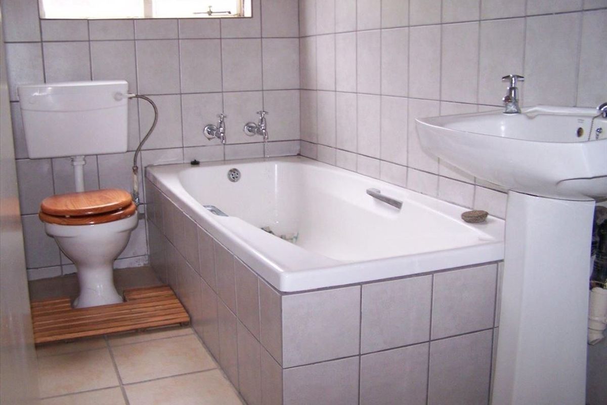 A functional bathroom featuring a standard bathtub, pedestal basin, and toilet with neutral wall and floor tiling.